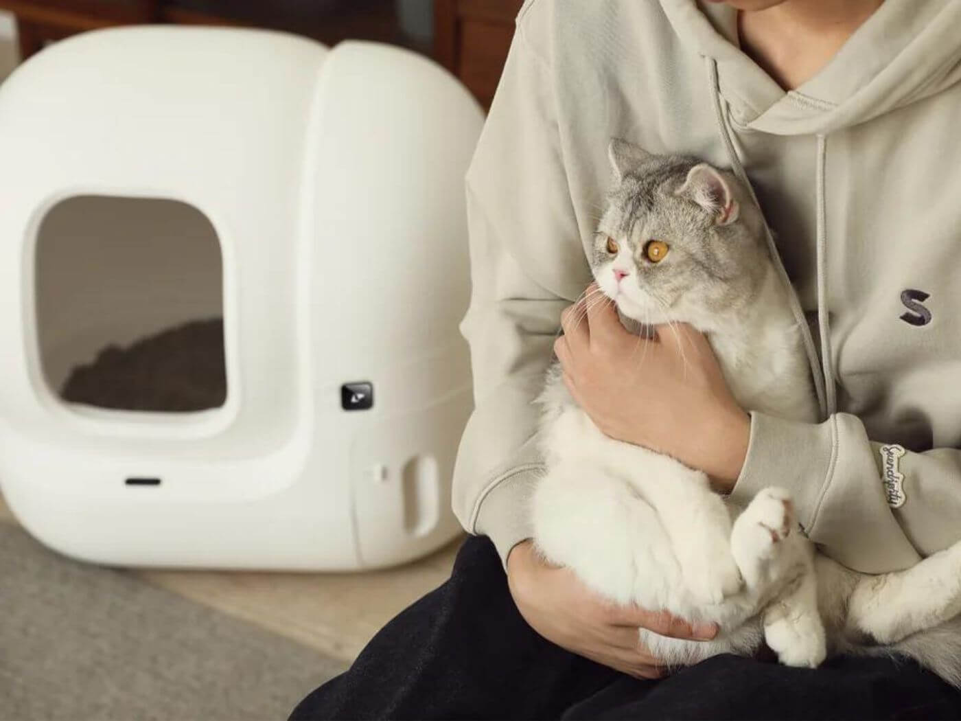 Katzenbesitzerin hält ihre Katze im Sitzen in ihren Armen und links von ihr ist das PETKIT Pura Max