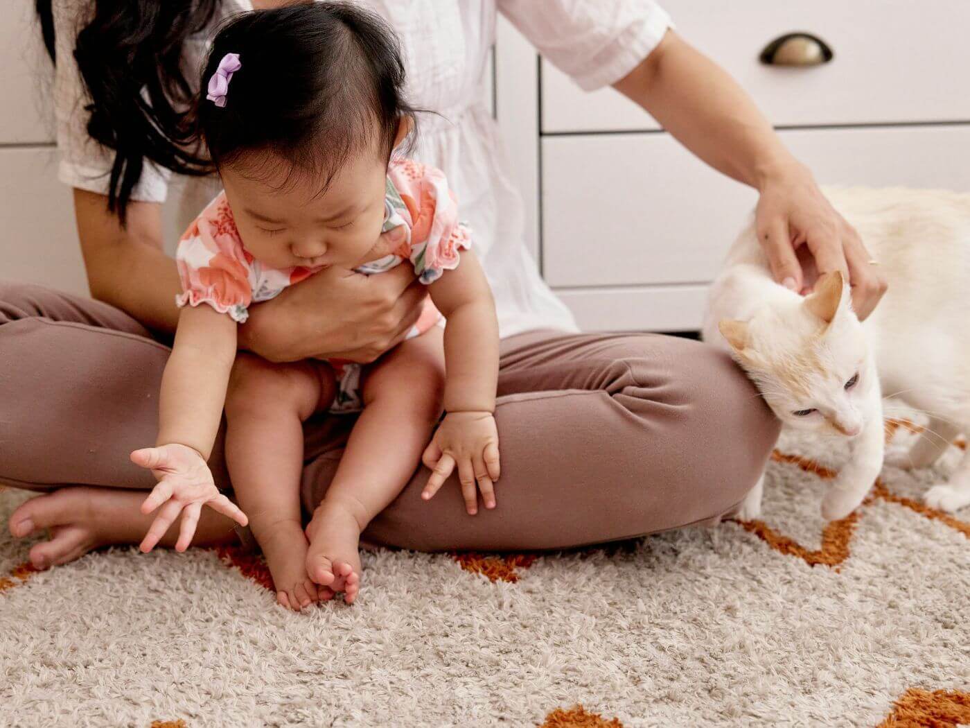 Mutter hält in einem Arm ihr Baby und mit ihrem anderem Arm streichelt sie ihre weiße Katze